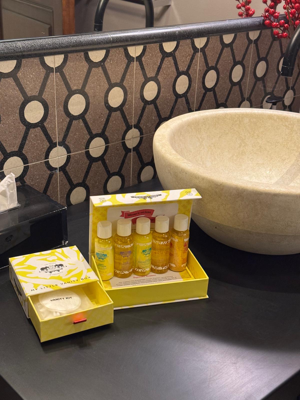 Hotel toiletries and vanity kit on a black counter beside a stone sink.