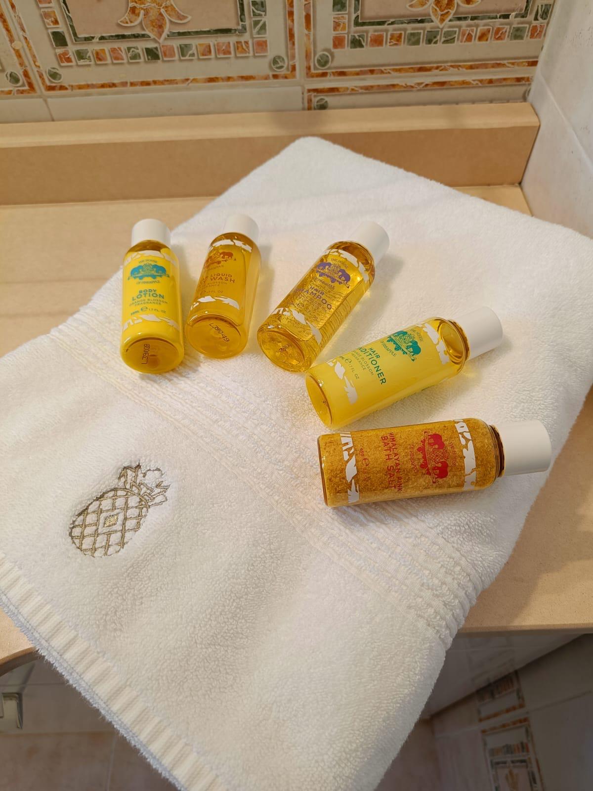 Mini toiletry bottles on a white towel with a pineapple design.
