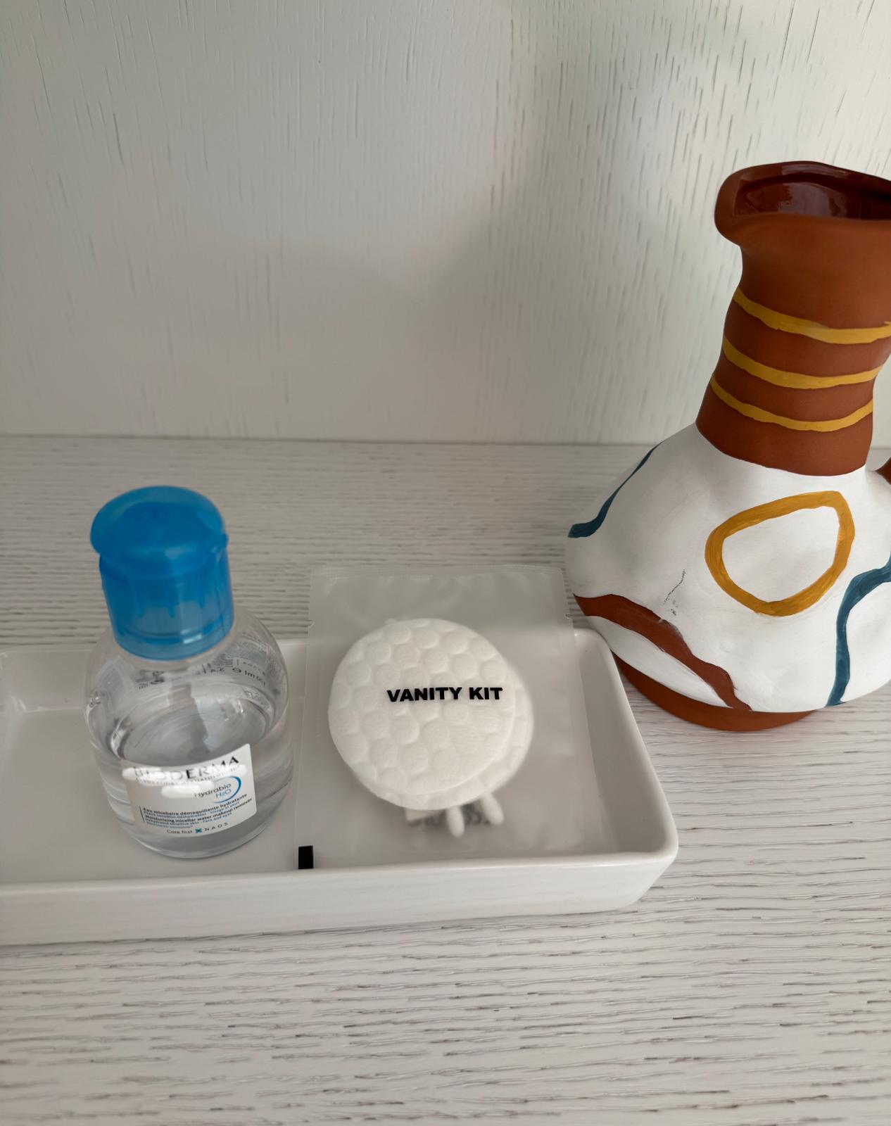 Vanity kit and a small bottle of liquid placed in a white tray next to a decorative ceramic jug.