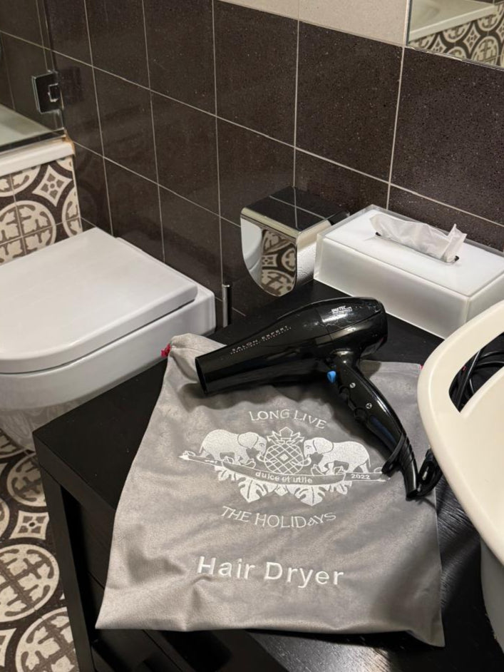 Hair dryer on branded pouch on bathroom counter near tissue box and toilet.